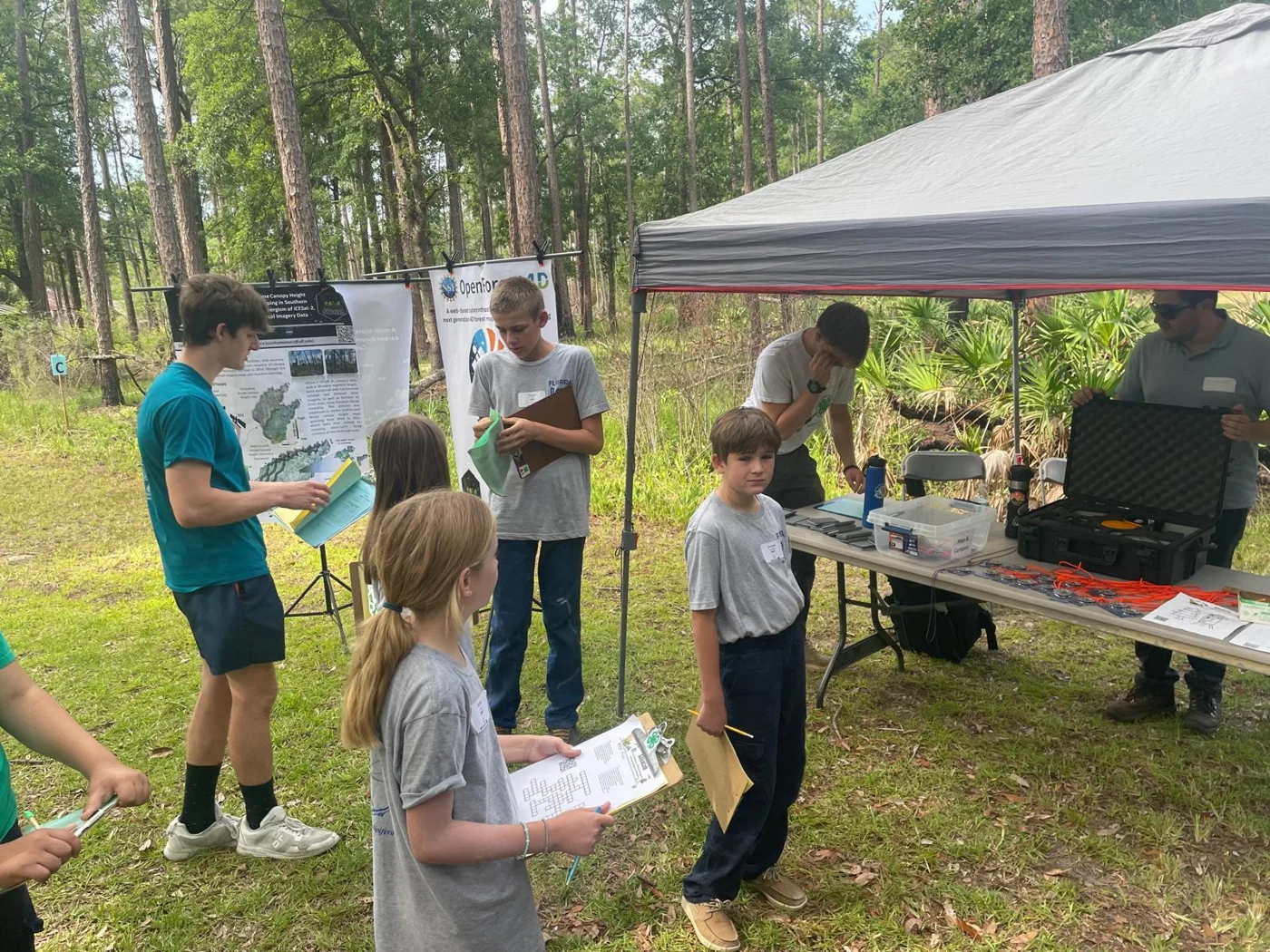Youth exploring forestry equipment and research at an outdoor station.